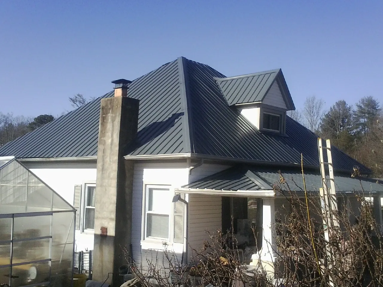 Dark blue standing seam metal roof on a white farmhouse with dormer — Slate & Tile Roof Repair by Roofing Brothers in Edgewood