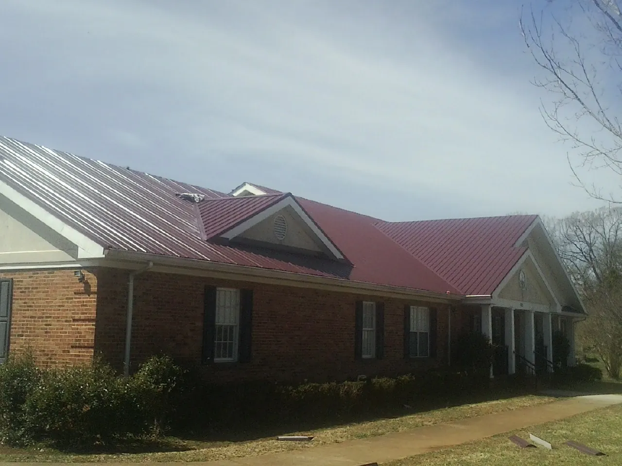 Red metal roof with gabled entries on a long brick building, from a Hail Damage Roof Repair job in Edgewood