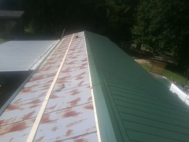Old rusted panels beside newly installed green metal roofing — Wind Damage Roof Repair by Roofing Brothers in Edgewood