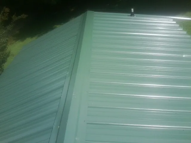 New green metal panels meeting at the ridge of a roof — Flat Roof Repair work by our crew in Edgewood