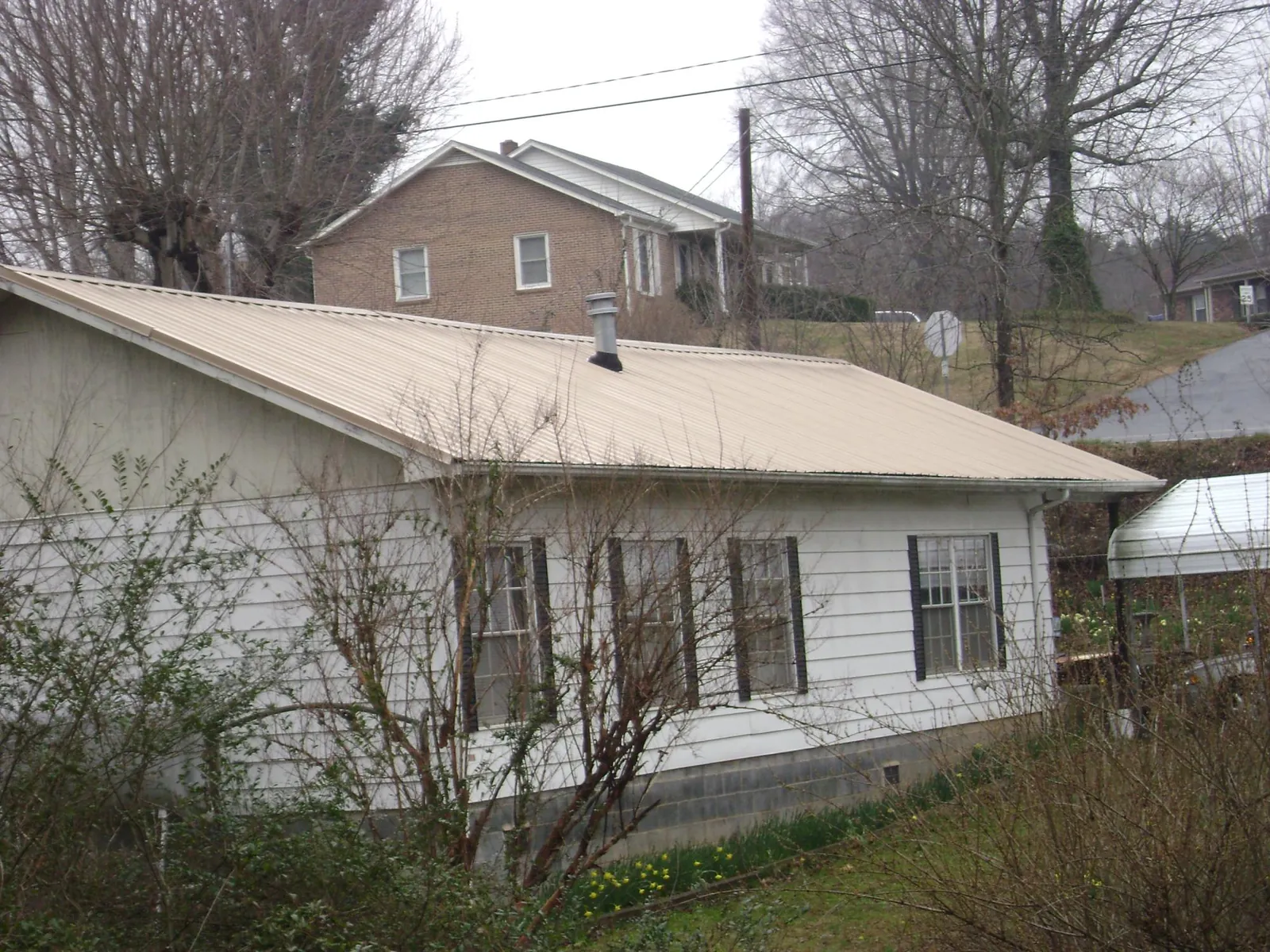 Tan metal roof on a white sided house set into a hillside — Commercial Roofing by Roofing Brothers in Edgewood
